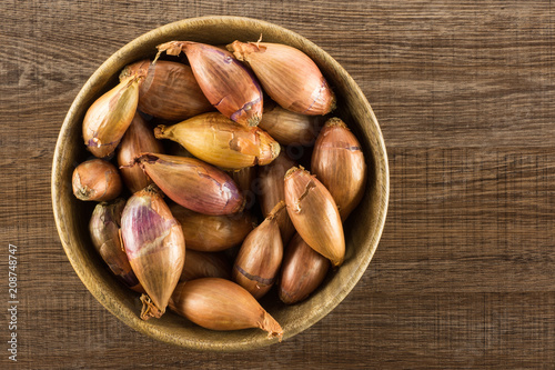 Long shallot in a wooden bowl top view isolated on brown wood background.