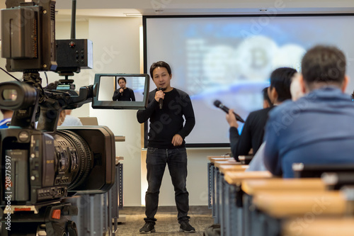 Closeup Video recording the Speaker with casual suit in front of the stage over Rear view of Audience in the conference hall or seminar meeting, event and education concept