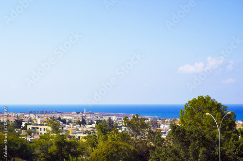 Landscape of town Paphos with houses, trees and sea in distance against blue sky