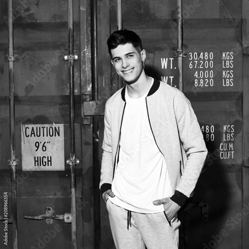 Young handsome sporty man in gary sport clothes posing against red metal doors of intermodal container