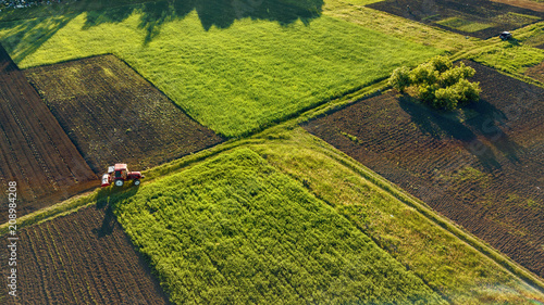 Aerial view from the drone, a bird's eye view of agricultural fields with a road through and a tractor on it in the spring evening at sunset