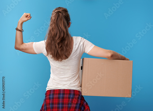 modern woman with cardboard box showing biceps on blue