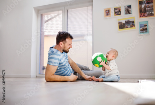 Young father playing with an unhappy baby son at home.