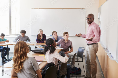 Male High School Tutor Standing At Whiteboard Teaching Class