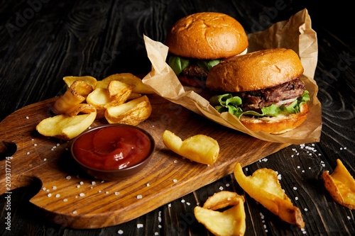 Tempting fast food diner with burgers and potatoes with sauce on cutting board