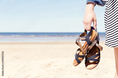 Woman on the beach holding her sandals at sunny summer day