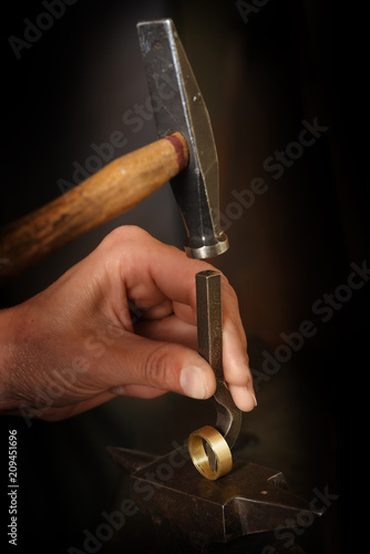 goldsmith hand punches a hallmark into a golden ring with a hammer on an anvil, copy space in the dark background