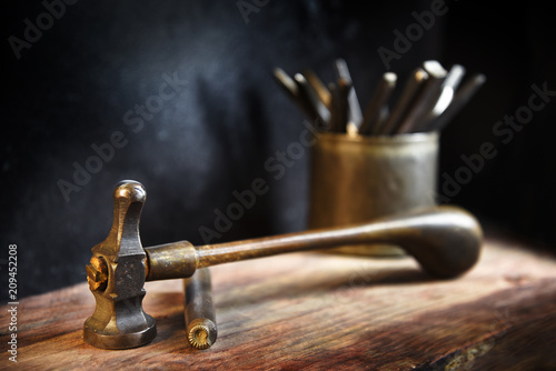vintage hammer and a hallmark steel punch, jewelry tools on a rustic wooden workbench of a goldsmith against a dark background with copy space