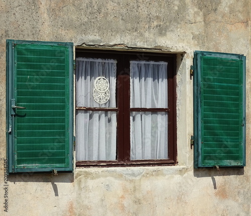 Okno z firanką i drewnainymi, ładnymi, w stylu vintage, zielonymi okiennicami z drewna, mur domu