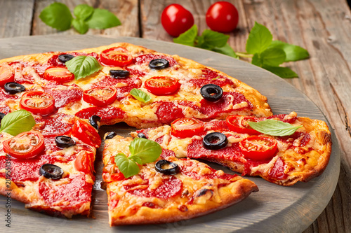 Pepperoni pizza with cherries tomatoes an olives on wooden table