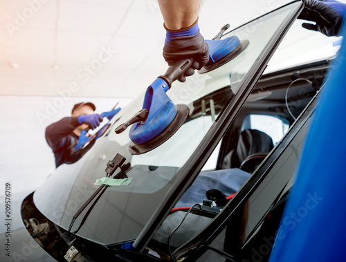 Automobile special workers replacing windscreen or windshield of a car in auto service station garage.