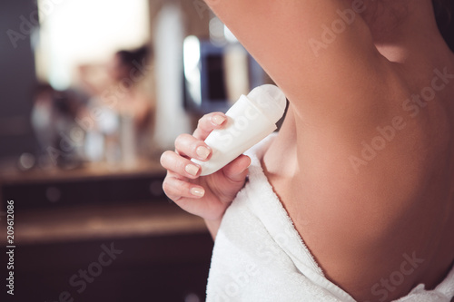 Close up of female hand preventing skin from perspiring. Girl is standing and holding antiperspirant in hand while rolling it on body