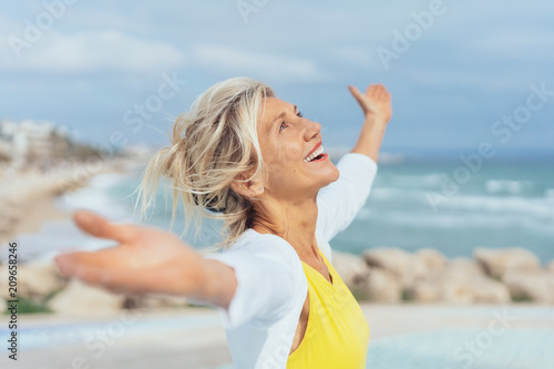 ältere Frau steht mit ausgebreiteten armen am strand und genießt den Urlaub