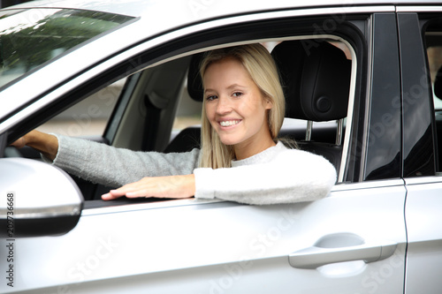 Hübsdche blonde Frau am Steuer eines Autos schaut lachend aus dem Fenster
