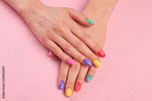 Female hands with colorful polish nails. Woman well-groomed hands with multicolor nails on salon table. Manicure nail painting.