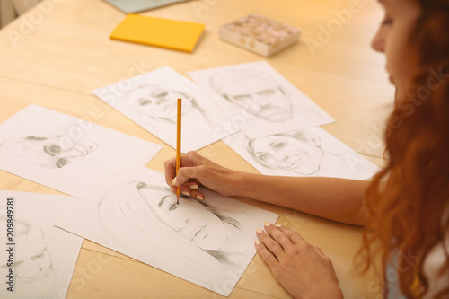 Drawing caricatures. Red-haired appealing creative person feeling extremely cheerful while drawing caricatures