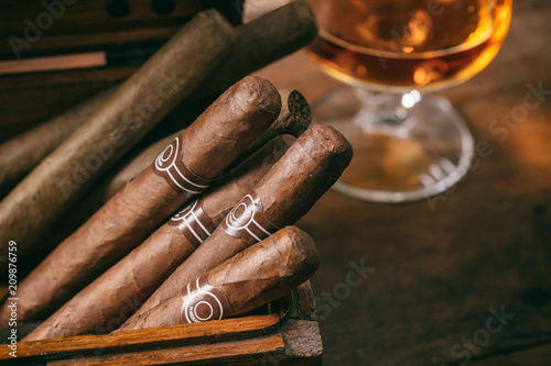 Cuban cigars closeup on wooden desk, blur glass of brandy