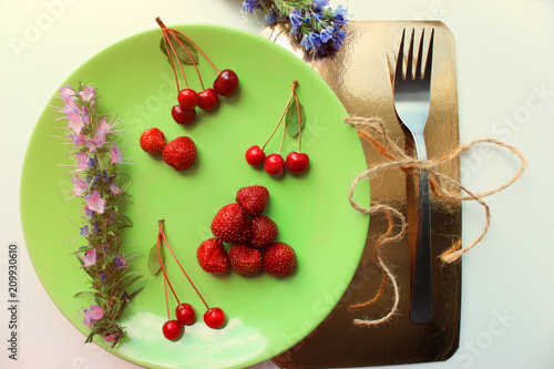Summer season. Vitamins cherries and strawberries on green plate. Wildflowers. Close up. Toning effect