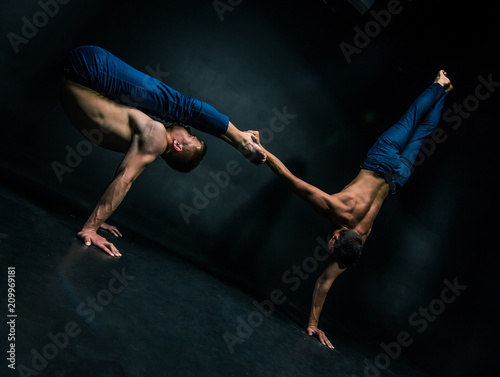 Male acrobatic duo performs a complicated balancing act on a dark background