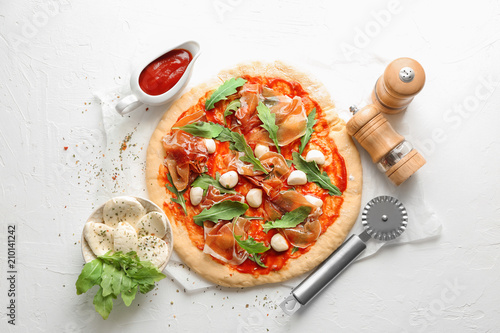 Raw pizza with tomato sauce and ingredients on light background