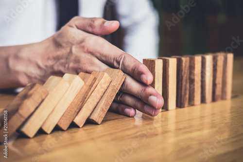 Strategy and successful intervention concept for business, businessman hand Stopping Falling wooden Dominoes effect from continuous toppled or risk