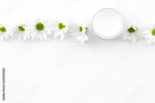 Chamomile cream. Face and body care. Cosmetics in small jar near chamomile flowers on white background top view copy space