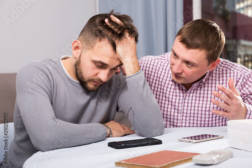 Friend calming distressed guy at home table