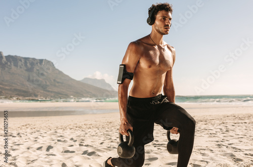 Man doing fitness training at the beach with kettlebells