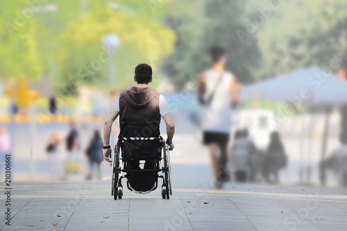 ASL affected young man on a wheel chair in the street among other people. Empty copy space for Editor's text.