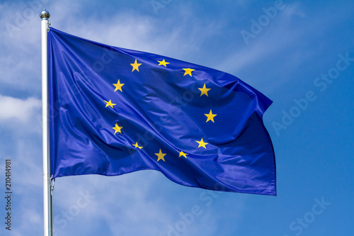 Flag of the European Union waving in the wind on flagpole against the sky with clouds on sunny day, close-up