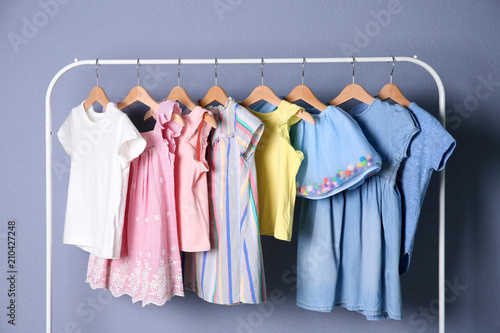 Rack with stylish child clothes on color background