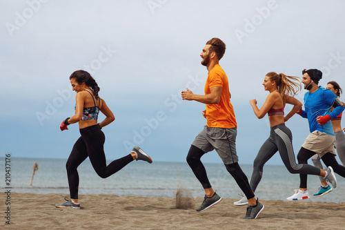 Group of young sports people running on the beach by the sea