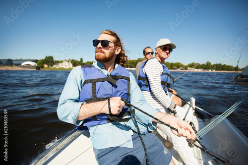 Group of men in protective lifejackets and sunglasses floating on yacht or motor boat on summer day