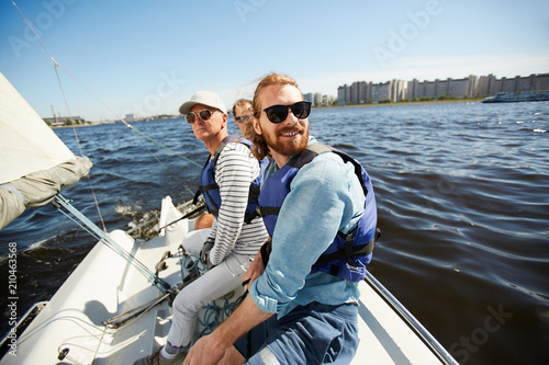 Active men in sunglasses sitting on yacht while floating in lake on hot summer day