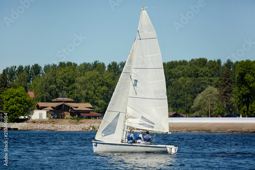 Three men sitting on yacht under sail and floating on water on hot summer day