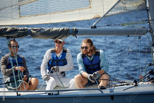 Team of three active men in lifejackets sitting in yacht while sailing in the sea