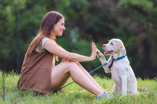 Beautiful young girl playing with a puppy labrador in the park 