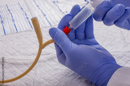 Nurse inflates urinary catheter bulb with leg drainage bag on sterile field.