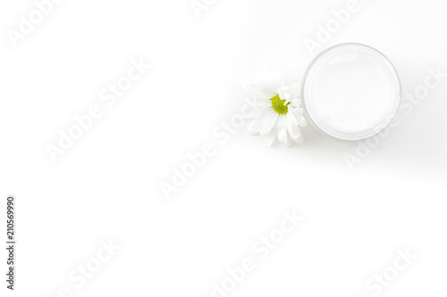Chamomile cream. Face and body care. Cosmetics in small jar near chamomile flowers on white background top view copy space