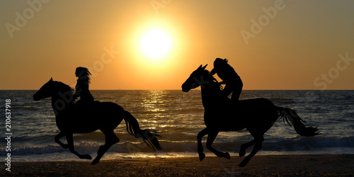 Two horse riders galloping on the beach