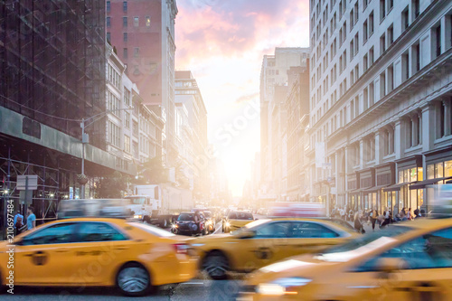 Taksówki w ruchu obok tłumów ludzi na Broadwayu z kolorowym zachodem słońca na Manhattanie w Nowym Jorku