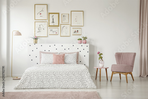 Feminine bedroom interior with white walls, polka dot bedding, pink elements and fashion drawings gallery in golden frames