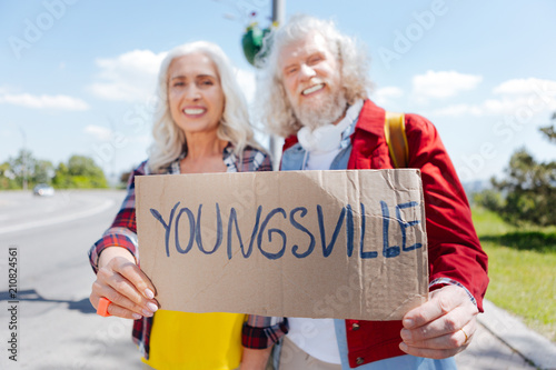 To Youngsville. Selective focus of a sign with an inscription being in hands of joyful non conformist couple