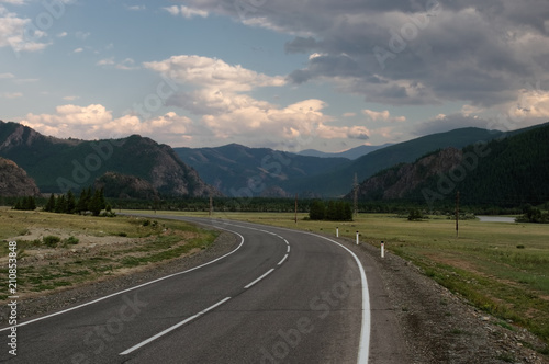 Road asphalt path at the background of the high mountain ranges under a dark dramatic sky Altai Mountains Siberia, Russia