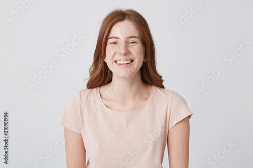 Portrait of cheerful beautiful young woman with freckles standing and smiling over white background