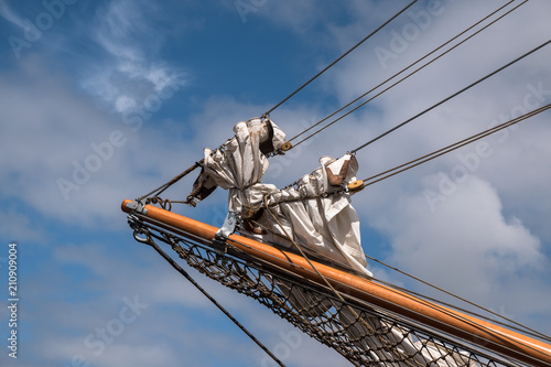 jib boom with reefed sails on the bow of a historic sailing ship against a blue sky with clouds, copy space