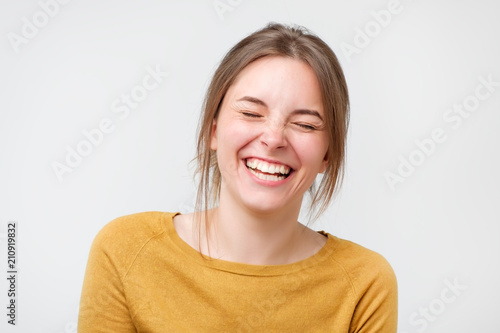 Beautiful young woman in yellow sweater laughing against white background.