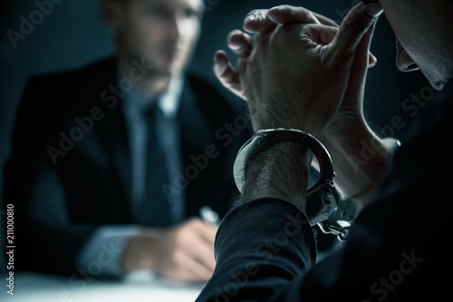 Criminal man with handcuffs in interrogation room