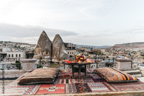 round table, pillows and traditional carpet on terrace and beautiful scenic of buildings and rocks in cappadocia, turkey
