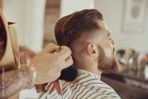 Barber shakes hair off from the client's neck. Photo in vintage style